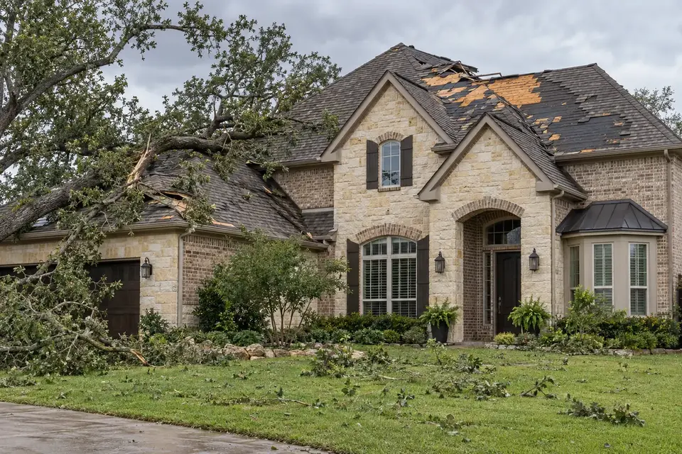 AI-generated illustration of an upscale stone home with wind-damaged shingles and a fallen tree limb
